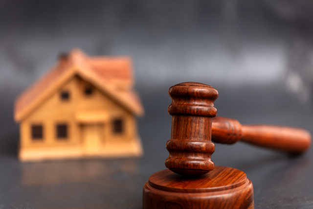 wooden-gavel-in-focus-with-a-small-model-house-in-the-background